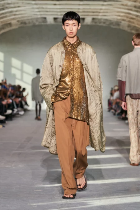 Model walking down the runway in a gold shirt.